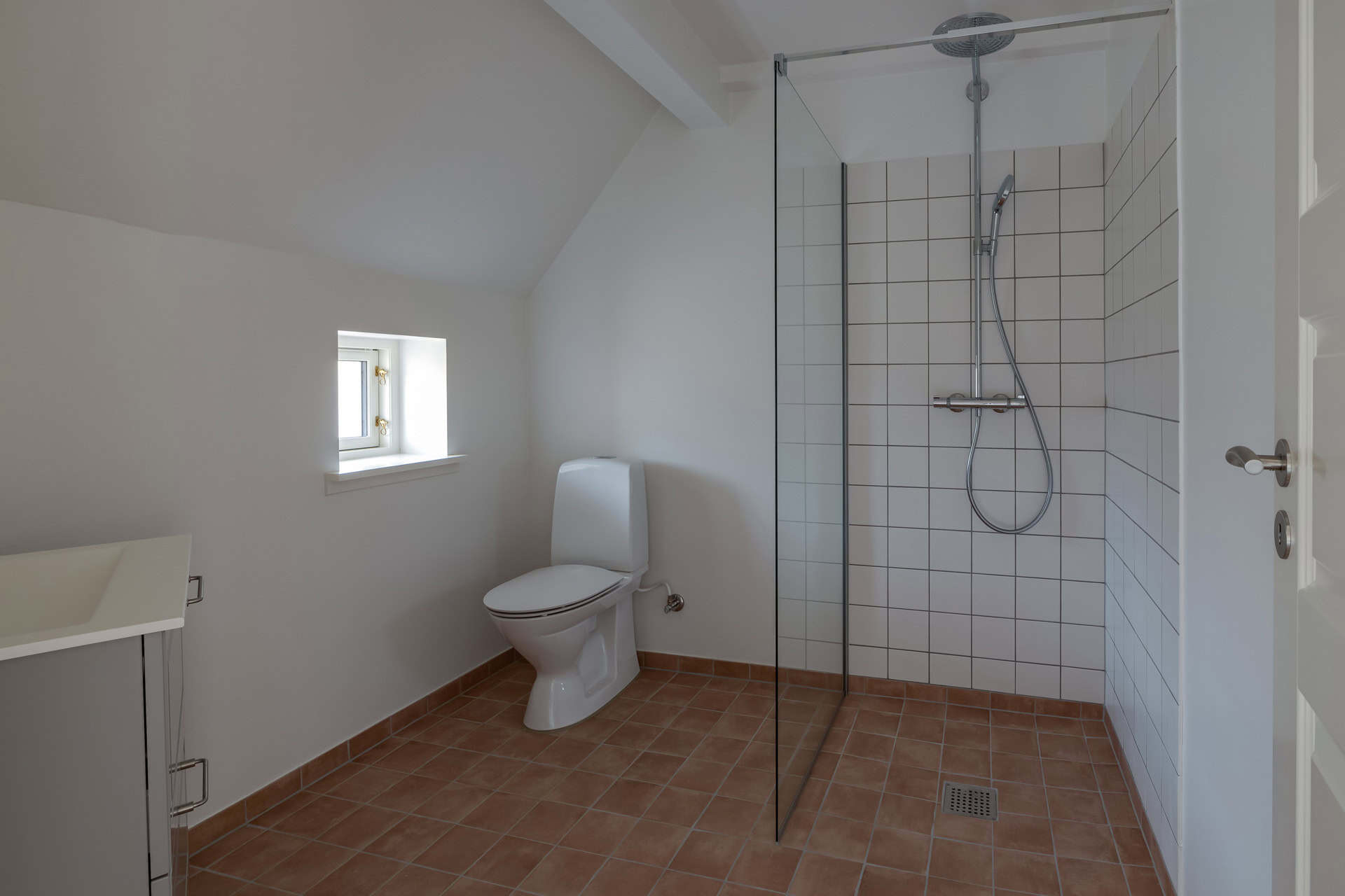 Toilet og bruseniche i hvidt badeværelse med skråvægge